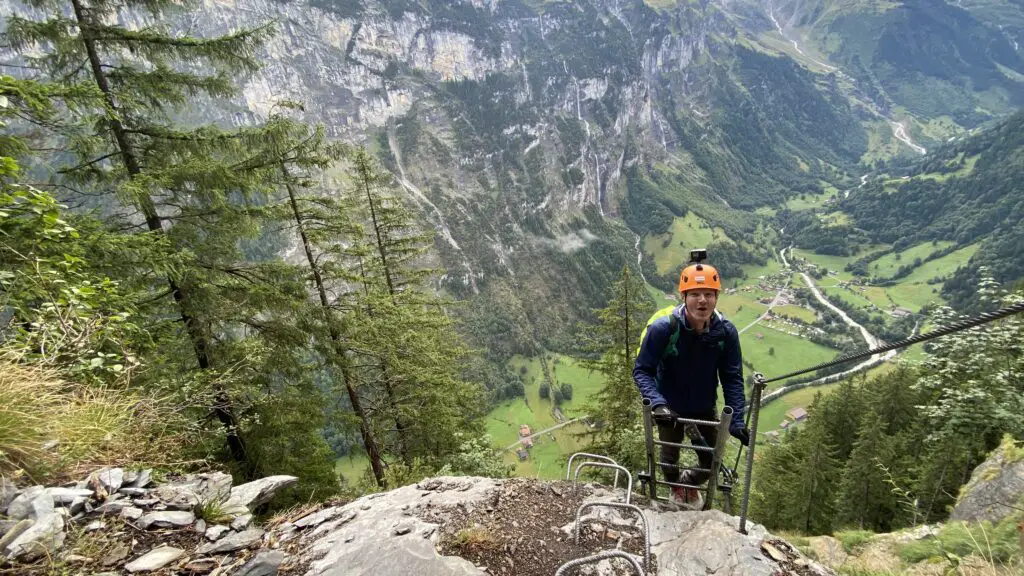Brett climbing down a ladder on the murren via ferrata with lauterbrunnen valley in the background 