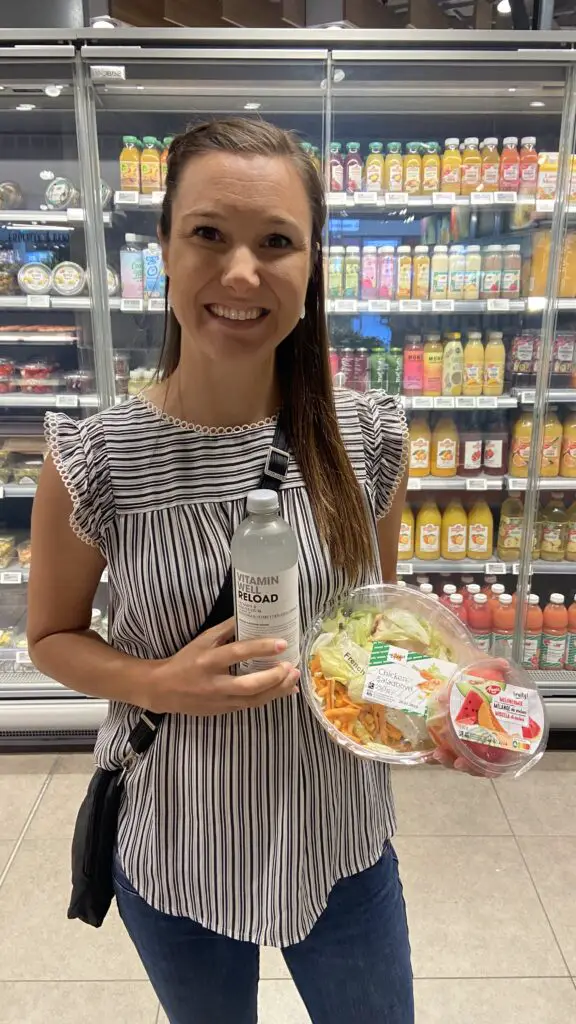 jana holding a caesar salad, fruit salad, and vitamin water from migros grocery store switzerland