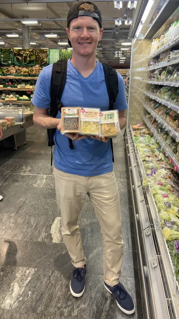 brett holding couscous, lentil salad, potato salad from coop grocery store in switzerland